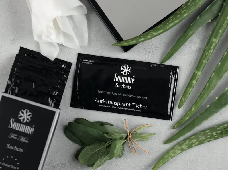 Produktfoto von Soummé: Anti-Transpirant-Tücher in schwarzen Sachets zwischen Salbei und Aloe vera